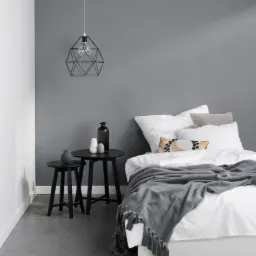 Minimalistyczna sypialnia z białą pościelą, szarym kocem z frędzlami, czarnymi stolikami nocnymi i geometryczną lampą wiszącą.