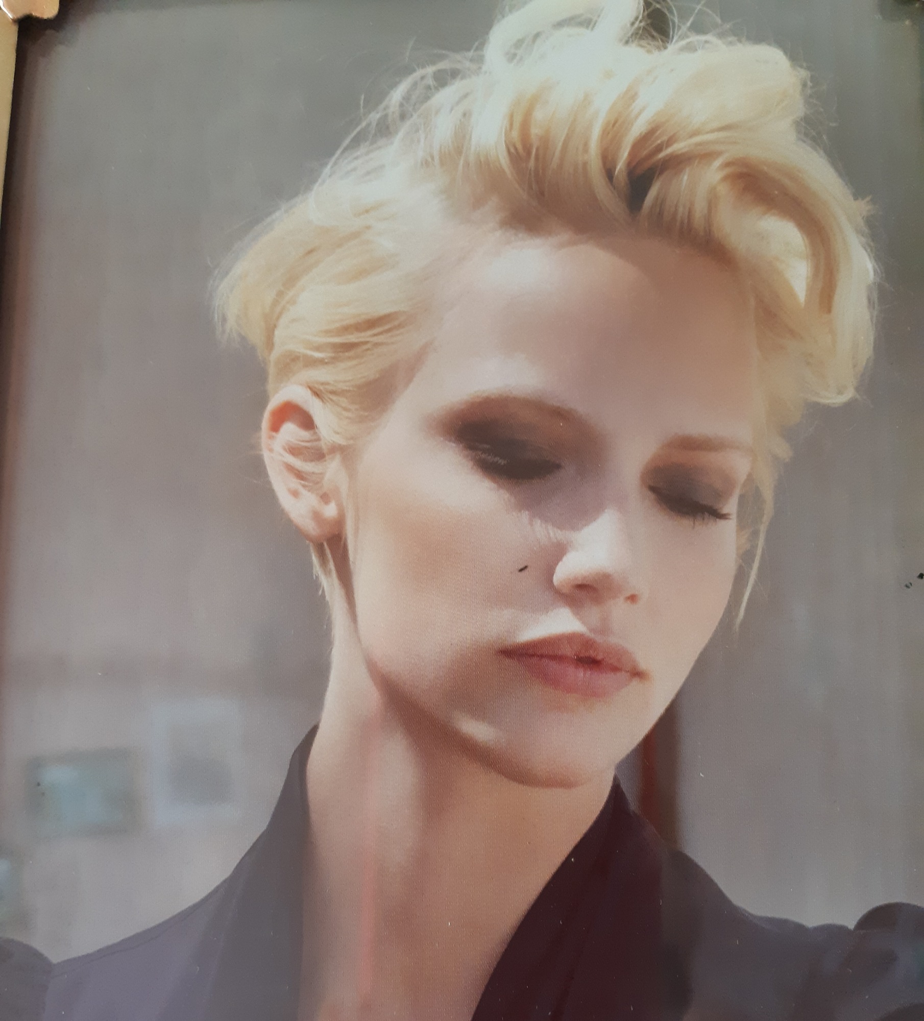 Portret kobiety z krótkimi, platynowymi włosami i mocnym makijażem oczu, spoglądającej w dół.