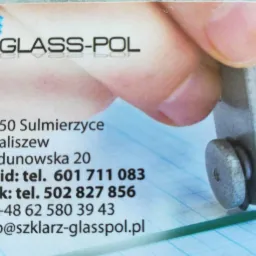 Wizytówka firmy Glass-Pol z adresem, numerami telefonów i adresem e-mail, obok której widać palec i narzędzie do cięcia szkła na tle siatki milimetrowej.