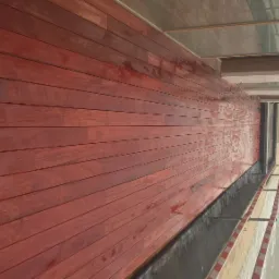 Czerwona drewniana podłoga tarasu z widokiem na morze, lekko mokra po deszczu, z fragmentem balustrady w czerwono-białe paski.