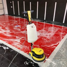 Usługi Sebastian Walczak - Czyszczenie podłogi przemysłowej za pomocą szorowarki Kärcher, widoczna piana i czerwona posadzka w trakcie mycia.