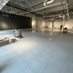 Usługi Sebastian Walczak - Wnętrze sklepu odzieżowego w trakcie sprzątania po remoncie, widoczna maszyna czyszcząca podłogę, resztki materiałów budowlanych i pracownik w tle.