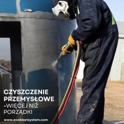 Usługi Sebastian Walczak - Pracownik w kombinezonie i masce ochronnej czyści metalową konstrukcję za pomocą strumienia pod ciśnieniem, widoczny efekt czyszczenia, przewód doprowadzający strumień w kolorze czerwono-żółtym.