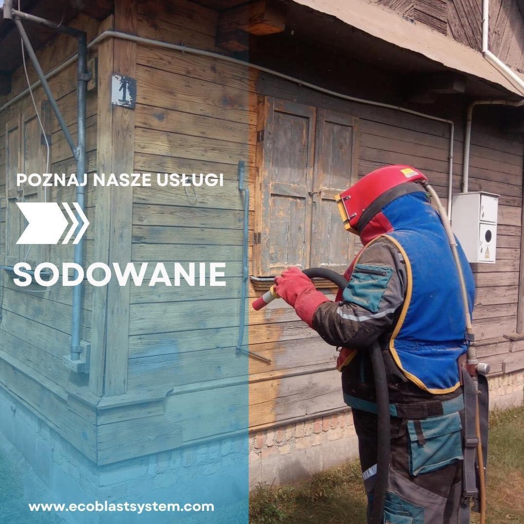 Pracownik w kombinezonie ochronnym soduje drewnianą elewację budynku, widoczna różnica w kolorze między obszarem przed i po czyszczeniu, na elewacji napis 'Poznaj nasze usługi SODOWANIE'.