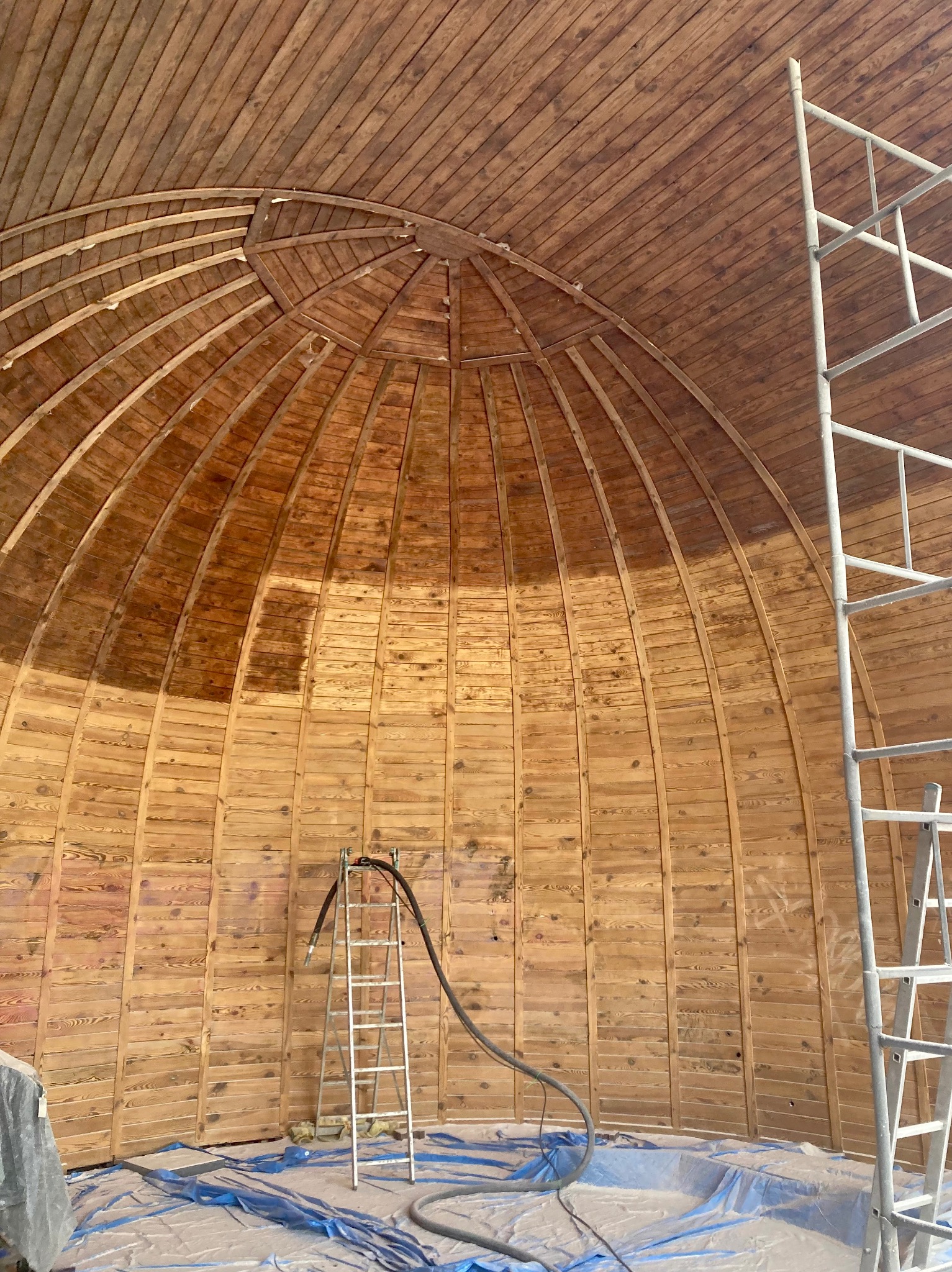 Wnętrze drewnianej kopuły w trakcie piaskowania, widoczne rusztowania, częściowo oczyszczona powierzchnia oraz zabezpieczająca folia na podłodze.