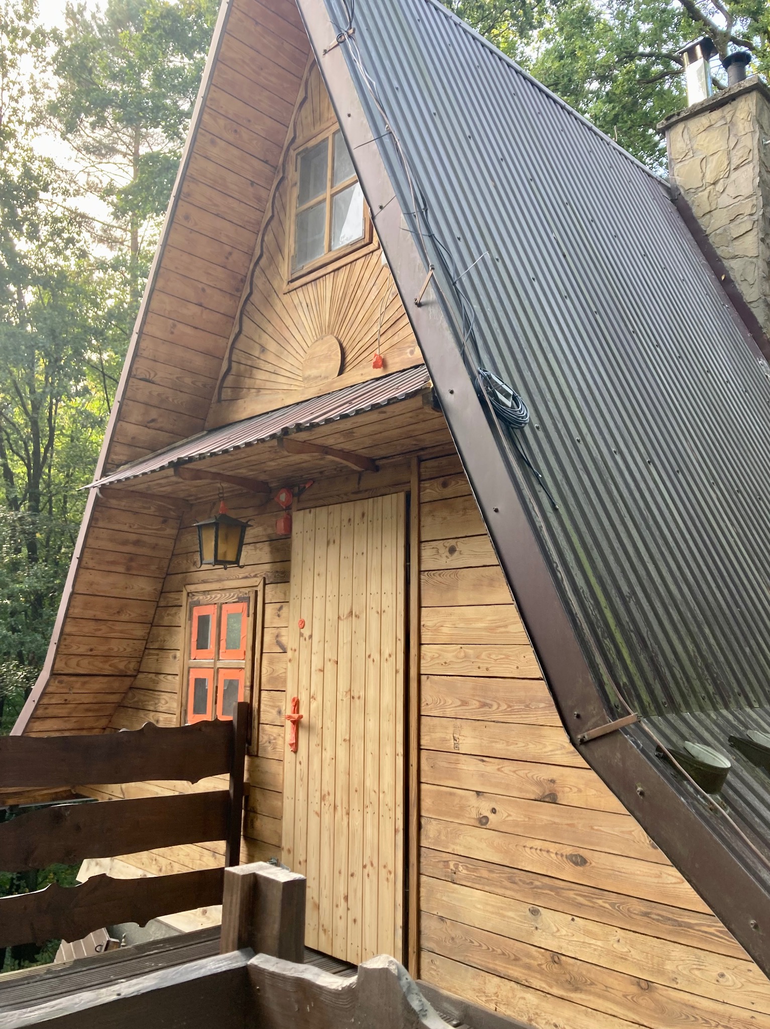 Drewniany dom w stylu góralskim z ciemną, metalową blachą na dachu, widoczny z dołu, z fragmentem balustrady balkonu.