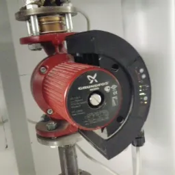 Czerwona pompa obiegowa Grundfos Magma zamontowana na metalowej rurze, z widocznymi diodami LED i tabliczką znamionową, w pomieszczeniu technicznym.