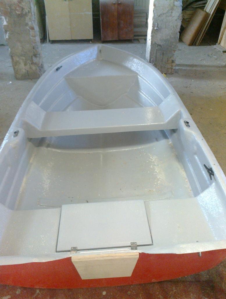 Wnętrze nowo pomalowanej, małej łódki wiosłowej z czerwonym dnem, widoczne z góry, z elementami sklejki i szarą farbą wewnątrz.