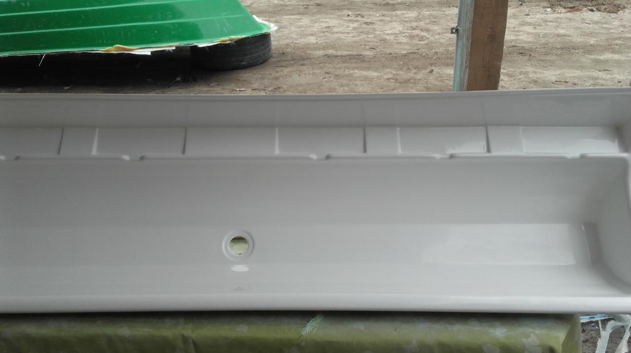 Biała, plastikowa wanna transportowa z widocznym otworem drenażowym, umieszczona na zielonej plandece, z fragmentem zielonej łodzi na oponie w tle