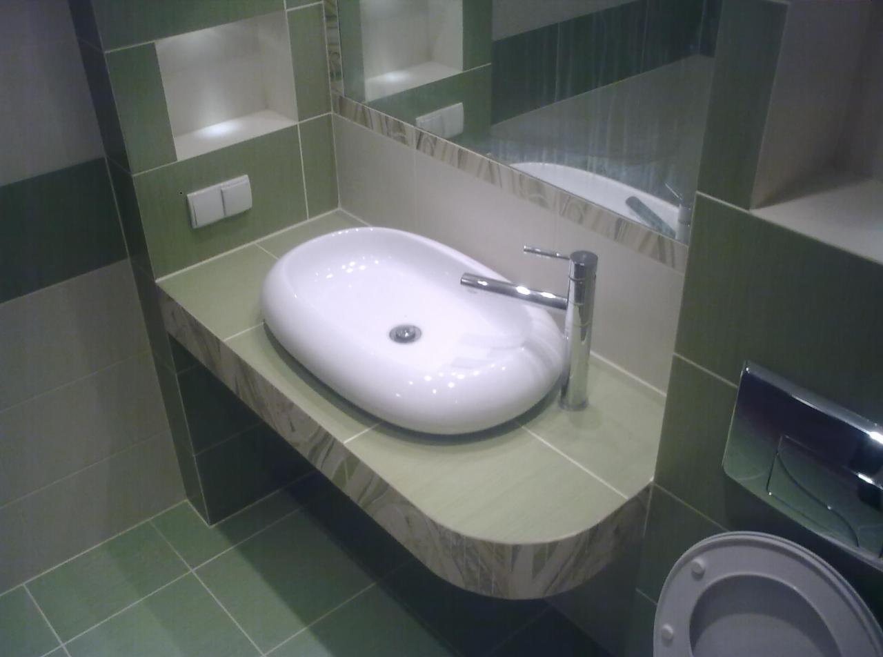 Nowoczesna łazienka z owalną umywalką nablatową, chromowaną baterią i zielono-białymi płytkami w tle.