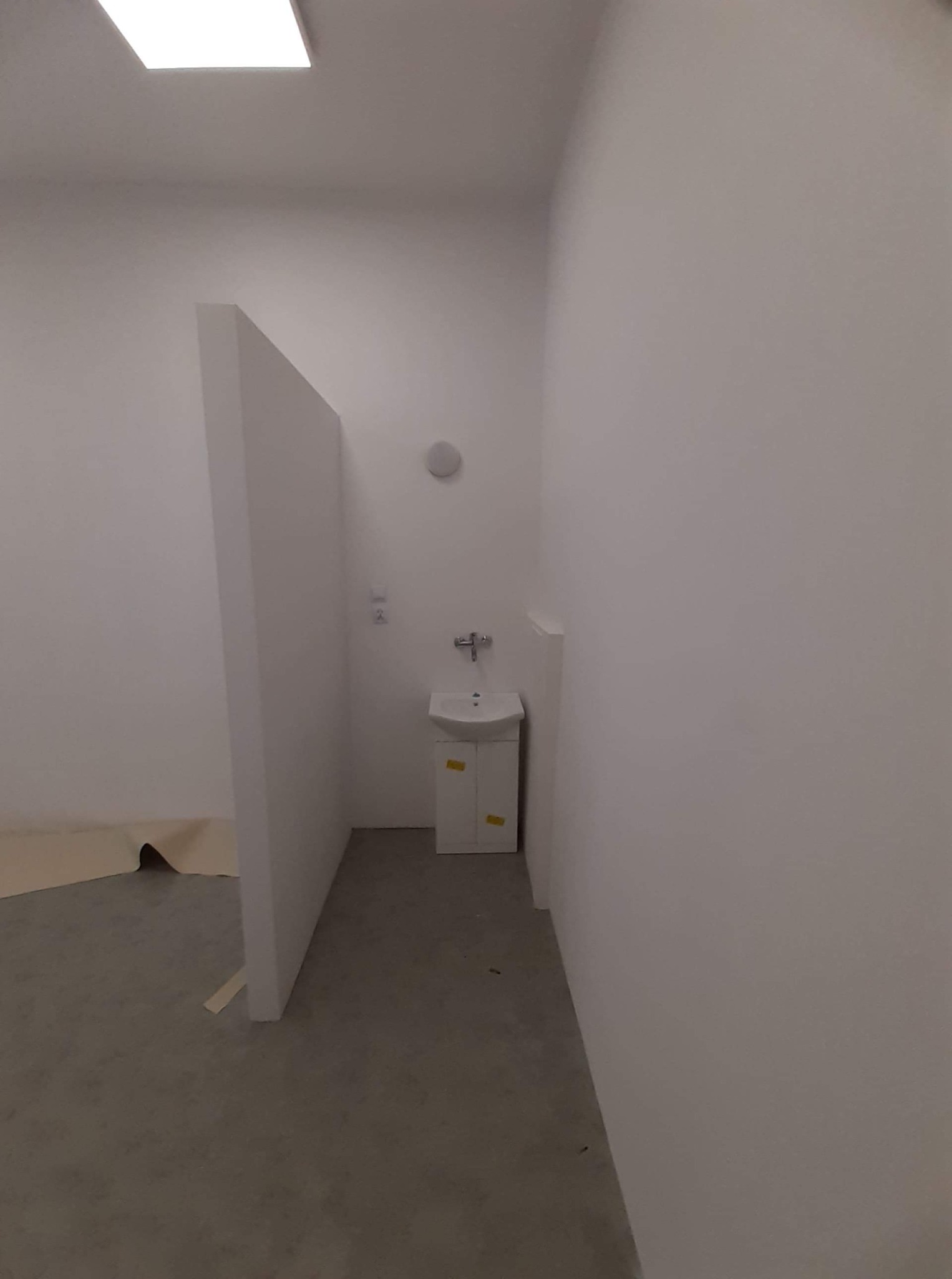 Białe pomieszczenie w trakcie remontu, z umywalką z szafką, ścianą działową i zabezpieczoną podłogą.