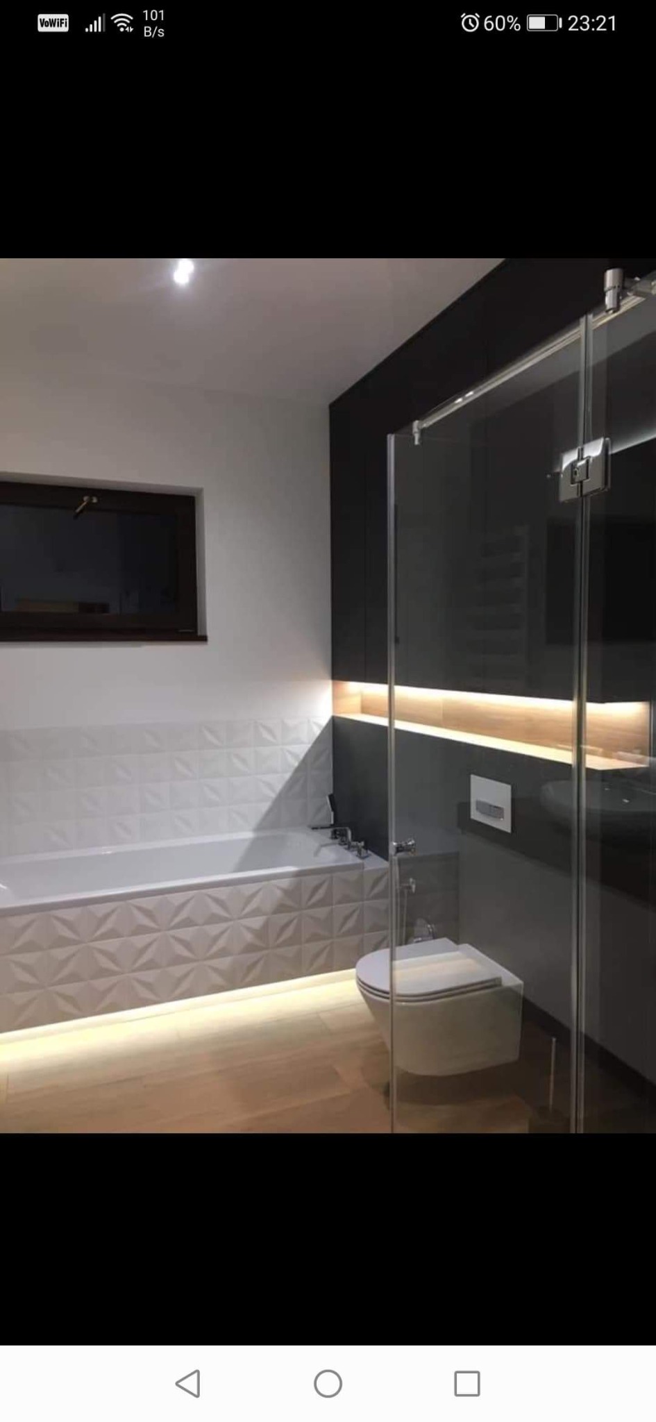 Nowoczesna łazienka z geometryczną białą glazurą, podświetlaną wanną, wiszącą toaletą i kabiną prysznicową ze szklanymi drzwiami przesuwnymi.