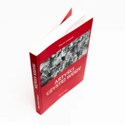 Otwarta książka w czerwonej twardej oprawie z czarno-białym zdjęciem na okładce, leżąca na białym tle pod kątem.