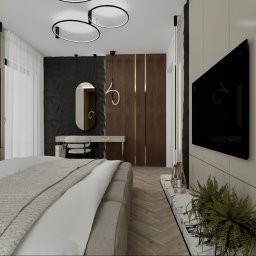 Inspiration Studio - Nowoczesna sypialnia z łóżkiem, toaletką z owalnym lustrem, telewizorem i dekoracyjną ścianą. Minimalistyczne oświetlenie i stonowana kolorystyka tworzą elegancki wystrój.
