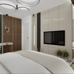 Inspiration Studio - Nowoczesna sypialnia z łóżkiem, toaletką z owalnym lustrem i telewizorem na ścianie. Drewniane panele i okrągłe lampy sufitowe dodają elegancji. Widok z perspektywy łóżka.