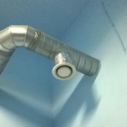 Klimaset - Metalowy kanał wentylacyjny z okrągłym wylotem na suficie w rogu pomieszczenia, widok z dołu.