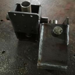 D1 - Dwa spawane elementy metalowe, jeden z rurą wewnątrz, leżące na metalowej powierzchni z widocznymi śladami obróbki.