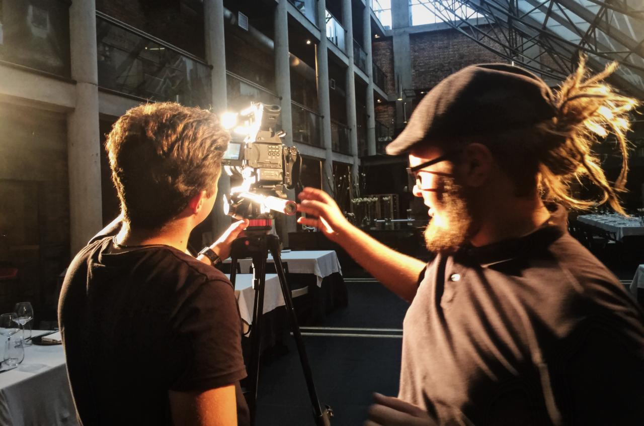 Ekipa filmowa z Katowic przygotowuje się do nagrania w industrialnym wnętrzu, widoczny operator z dredami i mężczyzna obsługujący kamerę na statywie.