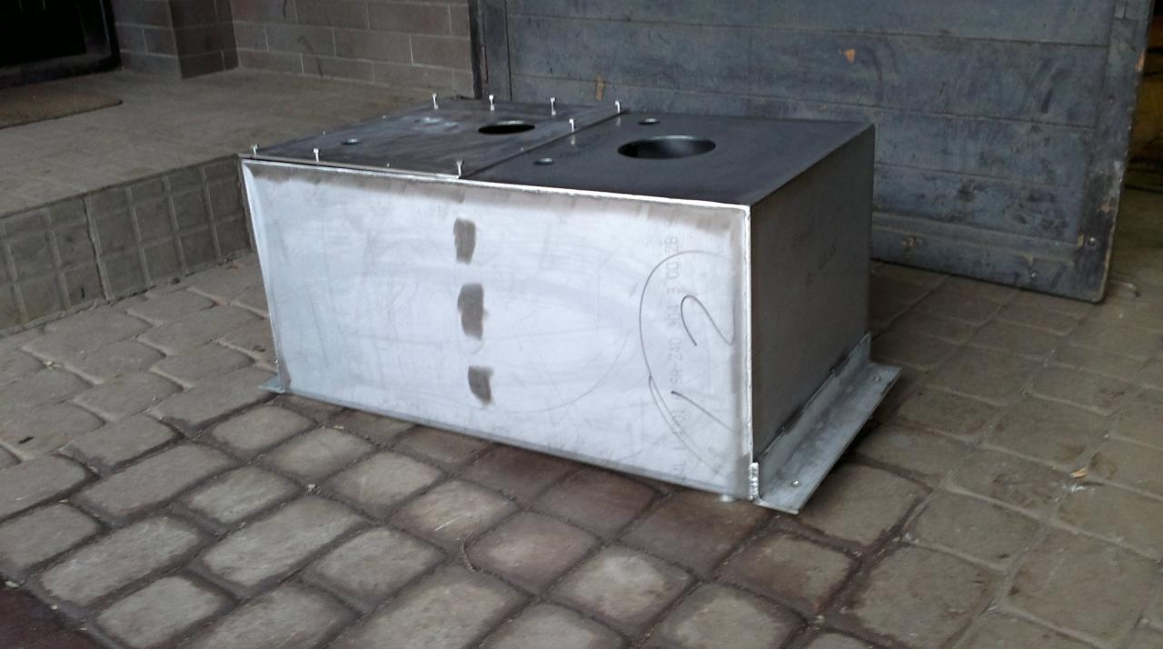 Surowy, metalowy pojemnik z otworami na górnej powierzchni, umieszczony na zewnątrz budynku w Krakowie, prawdopodobnie w trakcie produkcji lub montażu.