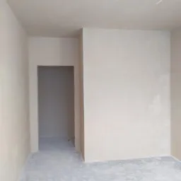 Pokój po szpachlowaniu z widocznym przejściem do innego pomieszczenia, surowy stan wykończenia podłogi.