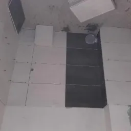 Świeżo ułożone, naprzemienne białe i grafitowe płytki na ścianie łazienki, z użyciem systemu poziomowania płytek (czerwone klipsy), widoczny fragment podłogi z niedokończonym kafelkowaniem i stertą...