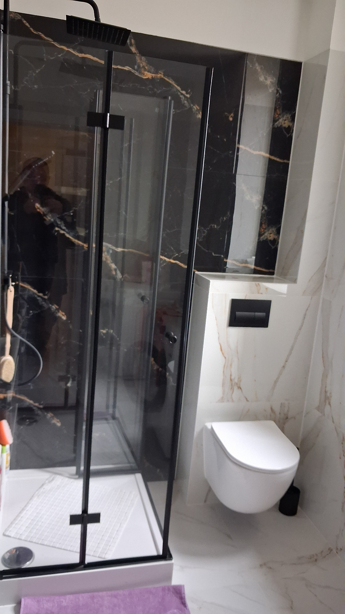 Wykończona łazienka w Gdańsku: kabina prysznicowa z czarnymi profilami i marmurowymi płytkami, podwieszana toaleta. Nowoczesny design i dbałość o detale.