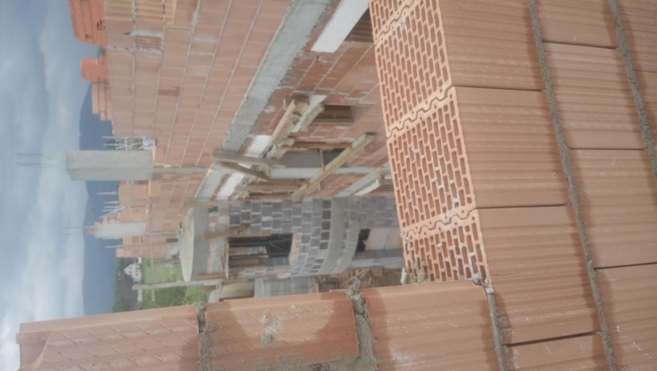 Wznoszenie ścian z czerwonej ceramiki poryzowanej, widoczne zbrojenie pionowe, w tle konstrukcje żelbetowe i krajobraz z górami.