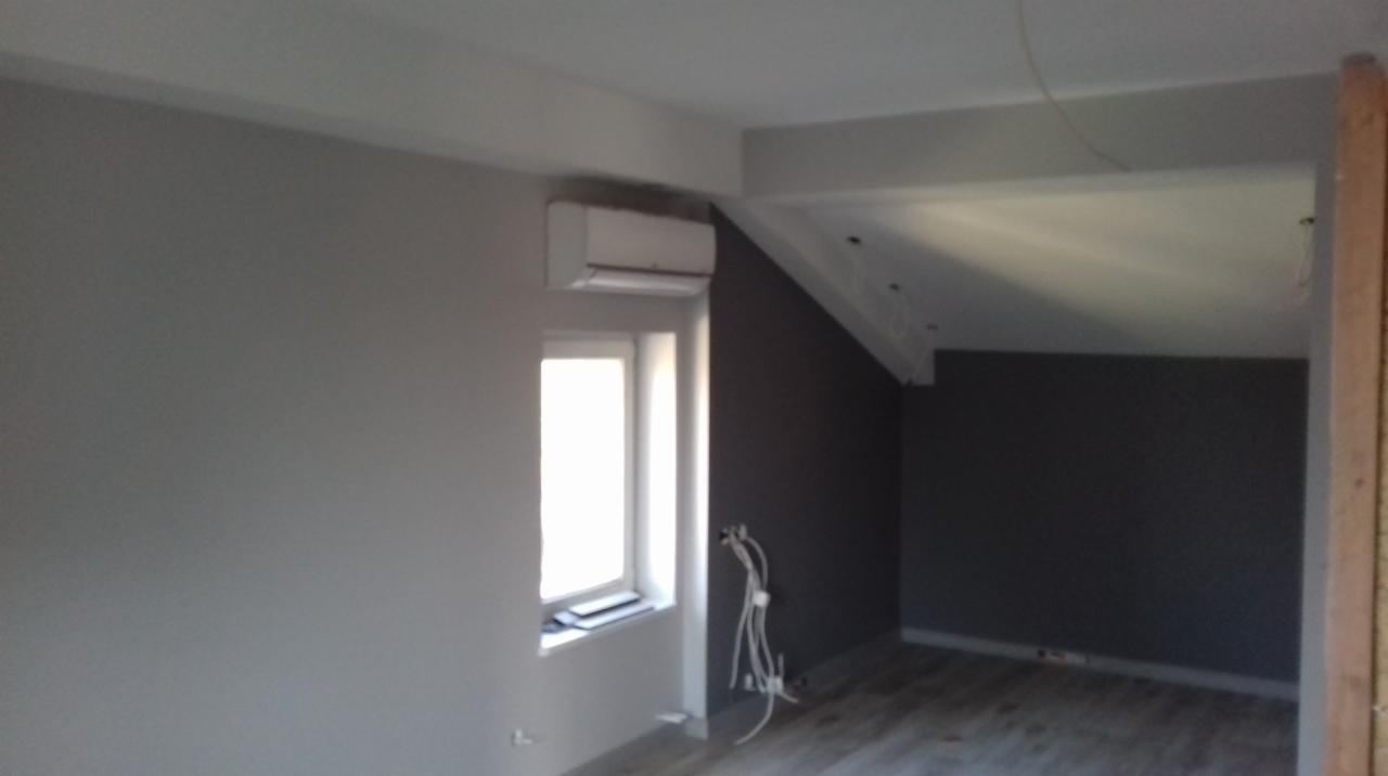 Szare poddasze po remoncie z zamontowanym klimatyzatorem, widoczne kable elektryczne i fragment drewnianej konstrukcji.