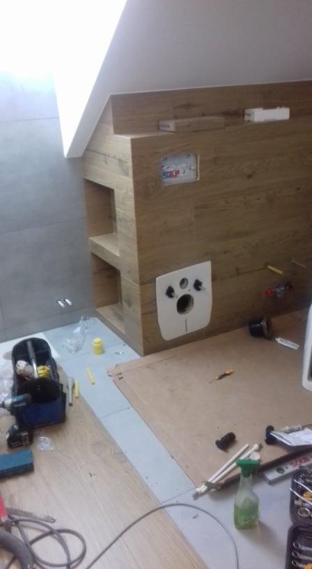 Montaż podtynkowego stelaża WC w obudowie z płyty drewnopodobnej, widoczne narzędzia i akcesoria instalacyjne na podłodze w trakcie prac.