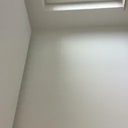 Świeżo pomalowane, jasne ściany w rogu pokoju z widocznymi otworami na kable elektryczne, oświetlenie sufitowe w tle.