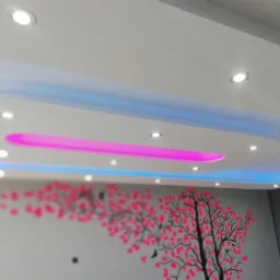 Sufit podwieszany z oświetleniem LED w kolorach niebieskim i różowym, z dekoracyjnym motywem drzewa z różowymi kwiatami na ścianie.