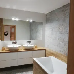 Nowoczesna łazienka w Warlubiu z dwoma umywalkami nablatowymi na drewnianym blacie, białe szafki pod umywalkami, wanna obudowana drewnem oraz ściana wykończona dekoracyjnymi płytkami w odcieniach...