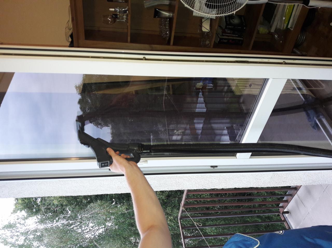 Czyszczenie okna z zewnątrz za pomocą specjalistycznego odkurzacza do okien z teleskopową rurą, widok z balkonu na zieleń.