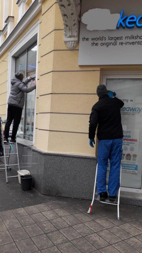 Dwie osoby na drabinach czyszczą okna i witrynę lokalu gastronomicznego z szyldem 'the world's largest milkshake'