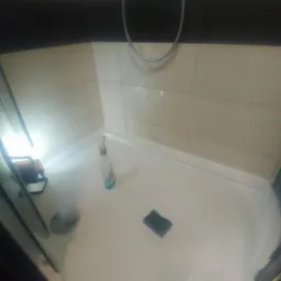 Brodzik kabiny prysznicowej po czyszczeniu, widoczna butelka środka czyszczącego i gąbka, oświetlone lampą roboczą.