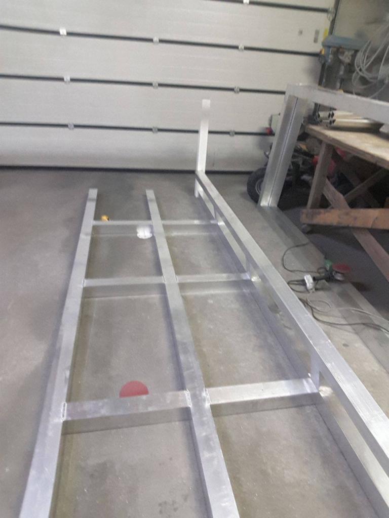 Stelaż z profili aluminiowych spawanych, widoczne spoiny, w tle brama garażowa i stół warsztatowy.