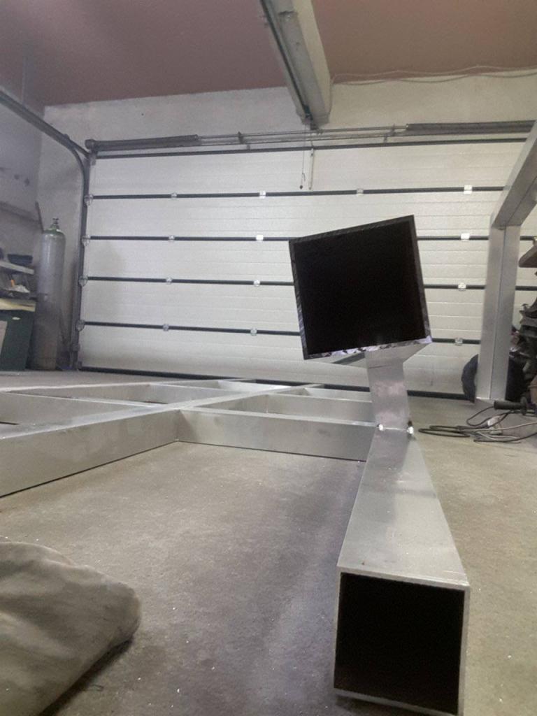 Konstrukcja spawana z profili aluminiowych o przekroju kwadratowym, widoczne spawy, tło stanowi brama garażowa.