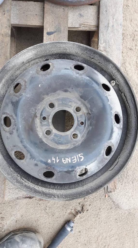 Brudna, stalowa felga samochodowa z napisem 'SIENA 14'' leżąca na drewnianej palecie, widoczne ślady korozji i zabrudzenia.