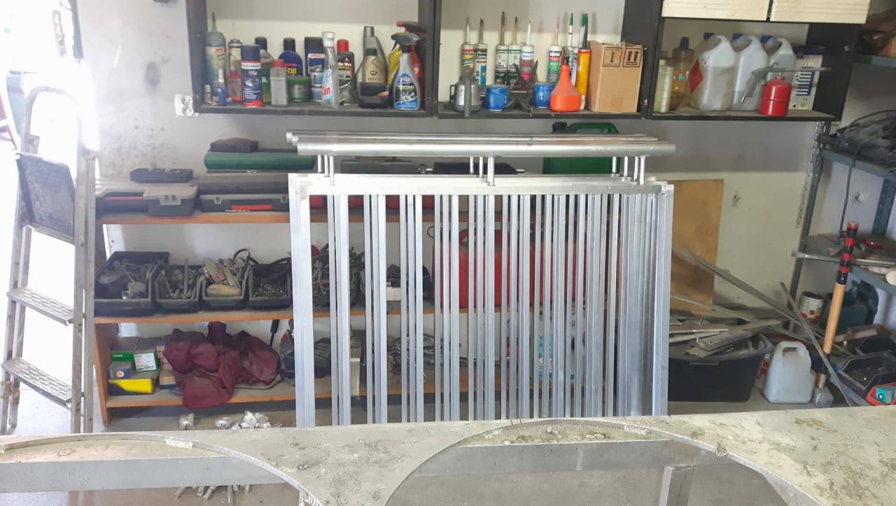 Aluminiowa konstrukcja balustrady z pionowymi prętami, w tle regały z narzędziami i materiałami w warsztacie.