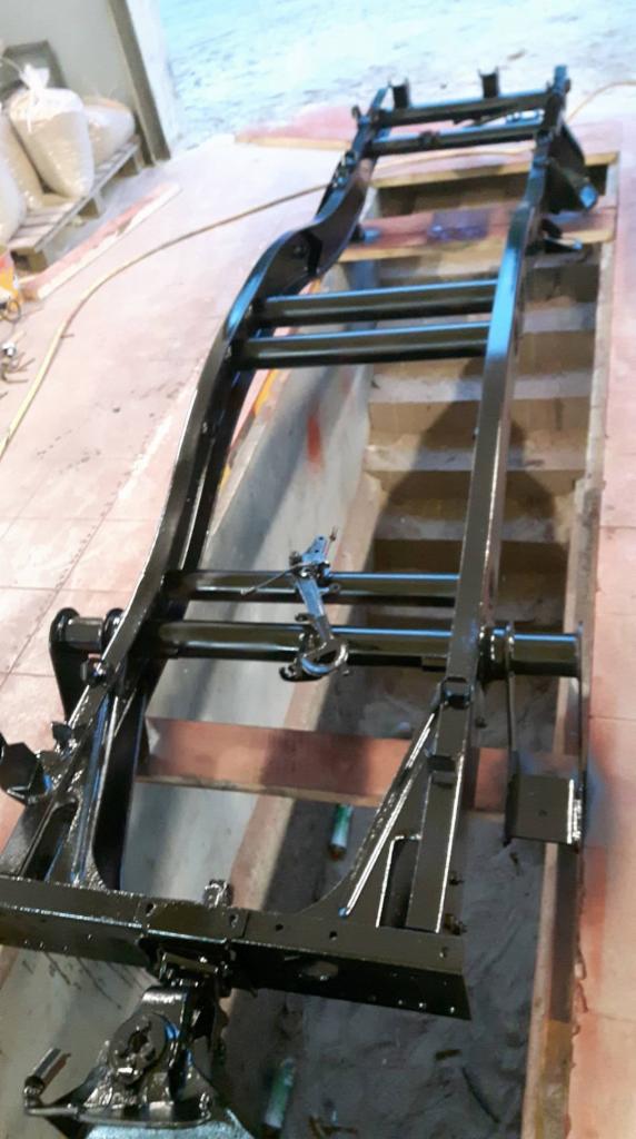 Czarna, metalowa rama pojazdu po renowacji, umieszczona na drewnianych belkach w warsztacie, widoczne detale konstrukcyjne i świeża powłoka lakiernicza.