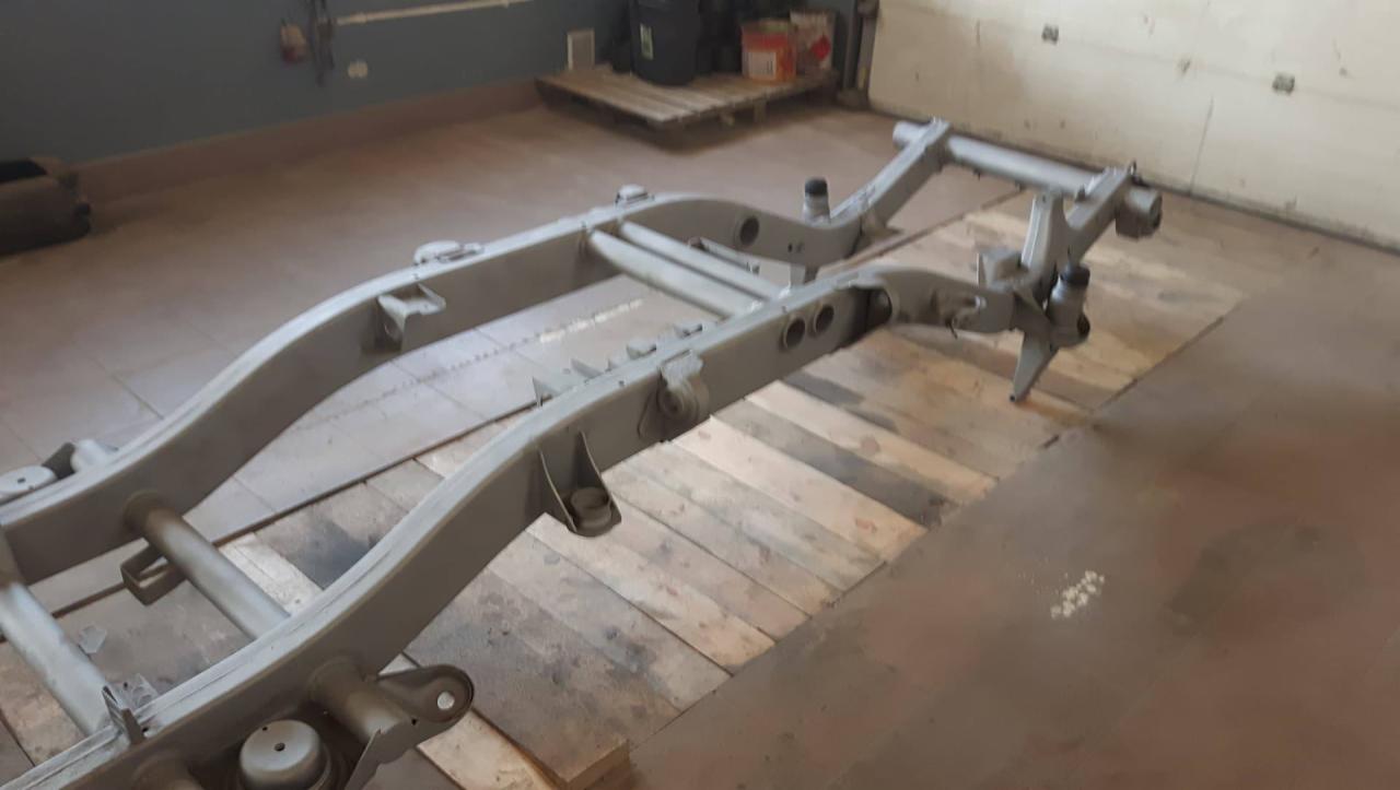 Pomarowana na szaro rama samochodu, leżąca na drewnianych paletach w warsztacie, widoczna z perspektywy lekko z góry.