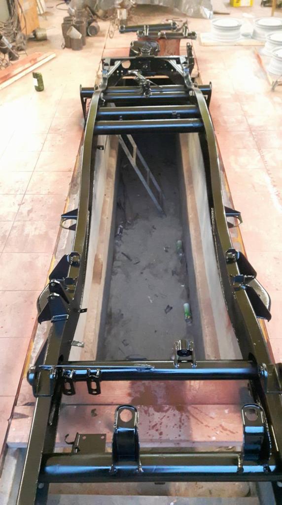 Odnowiona, czarna rama samochodu po piaskowaniu i malowaniu, widoczna nad kanałem warsztatowym.