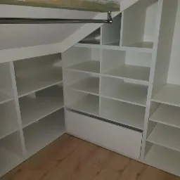 Biała szafa wnękowa z półkami i szufladą, dopasowana do skosu dachu, widok z wnętrza