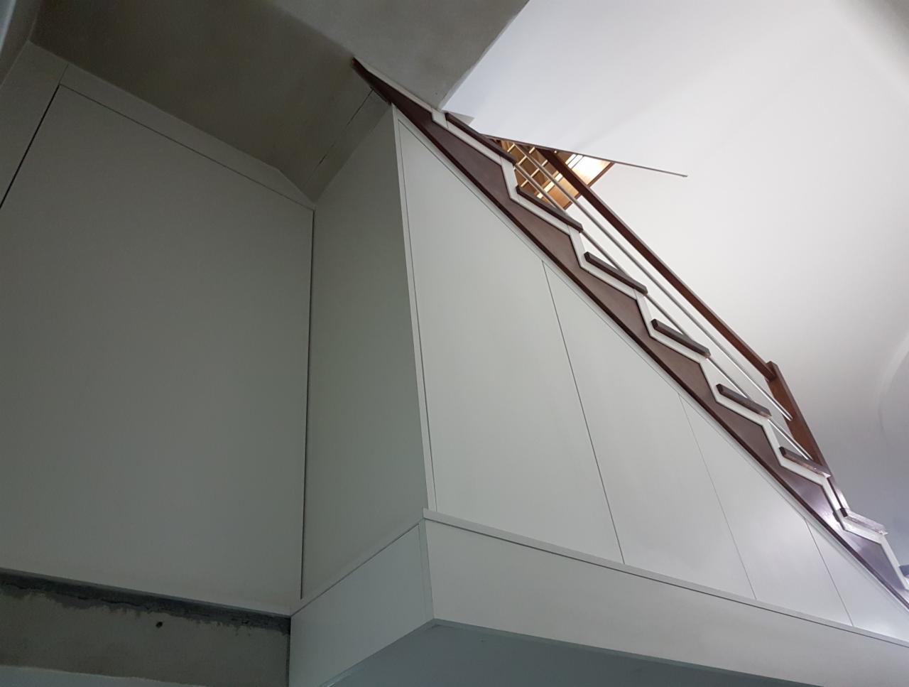 Biała zabudowa meblowa pod skosem dachu, z elementami dekoracyjnymi w kolorze brązowym, widoczna z dołu, w tle surowy beton