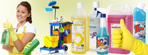 Uśmiechnięta kobieta w żółtych rękawicach i fartuchu trzymająca butelkę z rozpylaczem i gąbkę na tle wózka sprzątającego i różnych płynów czyszczących.