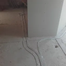 Wiązki przewodów elektrycznych ułożone na surowym betonowym podłożu w nowo budowanym pomieszczeniu z płyt kartonowo-gipsowych.