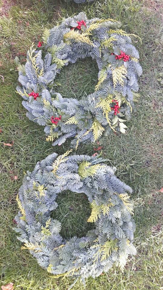 Dwa wieńce z gałęzi świerkowych i elementami ostrokrzewu z czerwonymi jagodami, leżące na trawie.