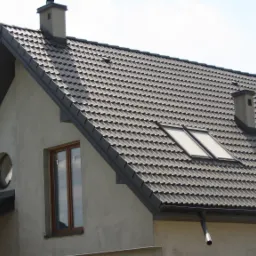 Nowy dach z ciemnej dachówki ceramicznej z dwoma oknami dachowymi i kominem na domu jednorodzinnym.