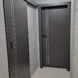 Dwie szare konstrukcje: przesuwne skrzydło z bocznym zamkiem i uchwytem oraz tradycyjne skrzydło z czarną klamką, obie z pionowymi, srebrnymi paskami, na tle szarej ściany o nierównej fakturze...