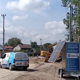 Grupa Oktagon Sp. z o.o. - Biała furgonetka serwisowa OKTAGON i mobilna wieża monitorująca z panelami słonecznymi i kamerami na placu budowy z koparką w tle.